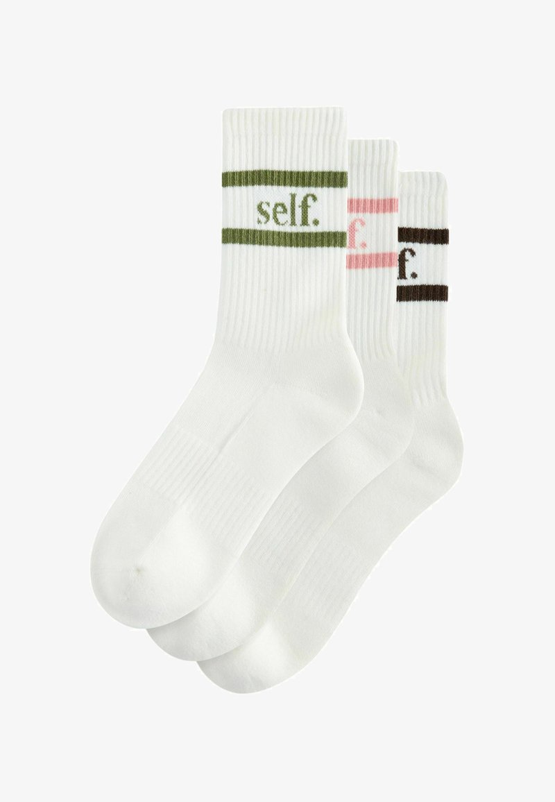 Drei Paar weiße Socken mit geripptem Muster. Jede Socke hat einen farbigen Streifen – grün, rosa und braun – und das Wort "self." in Kleinbuchstaben.