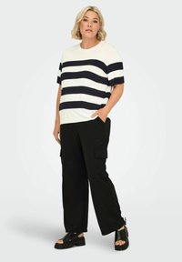 Maglione a righe bianco e navy, maniche corte. Abbinato a pantaloni cargo neri con tasche laterali e sandali platform neri con lacci.
