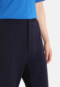 Marinblå joggingbyxor gjorda av mjukt tyg, med elastisk midja, sidofickor och en avslappnad passform med synliga sömdetaljer.