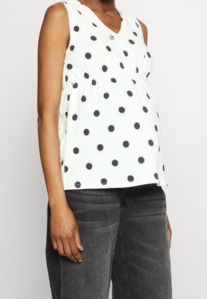 Top blanco sin mangas con lunares negros, con escote en V y cintura fruncida. Combinado con vaqueros gris oscuro.