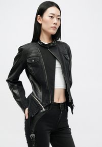 Mustast nahast mootorratturi jope, millel on asümeetriline tõmblukk, kaks esipocketit ja tekstuuripaneelid külgedel. Kanda lühikese valge särke peal.