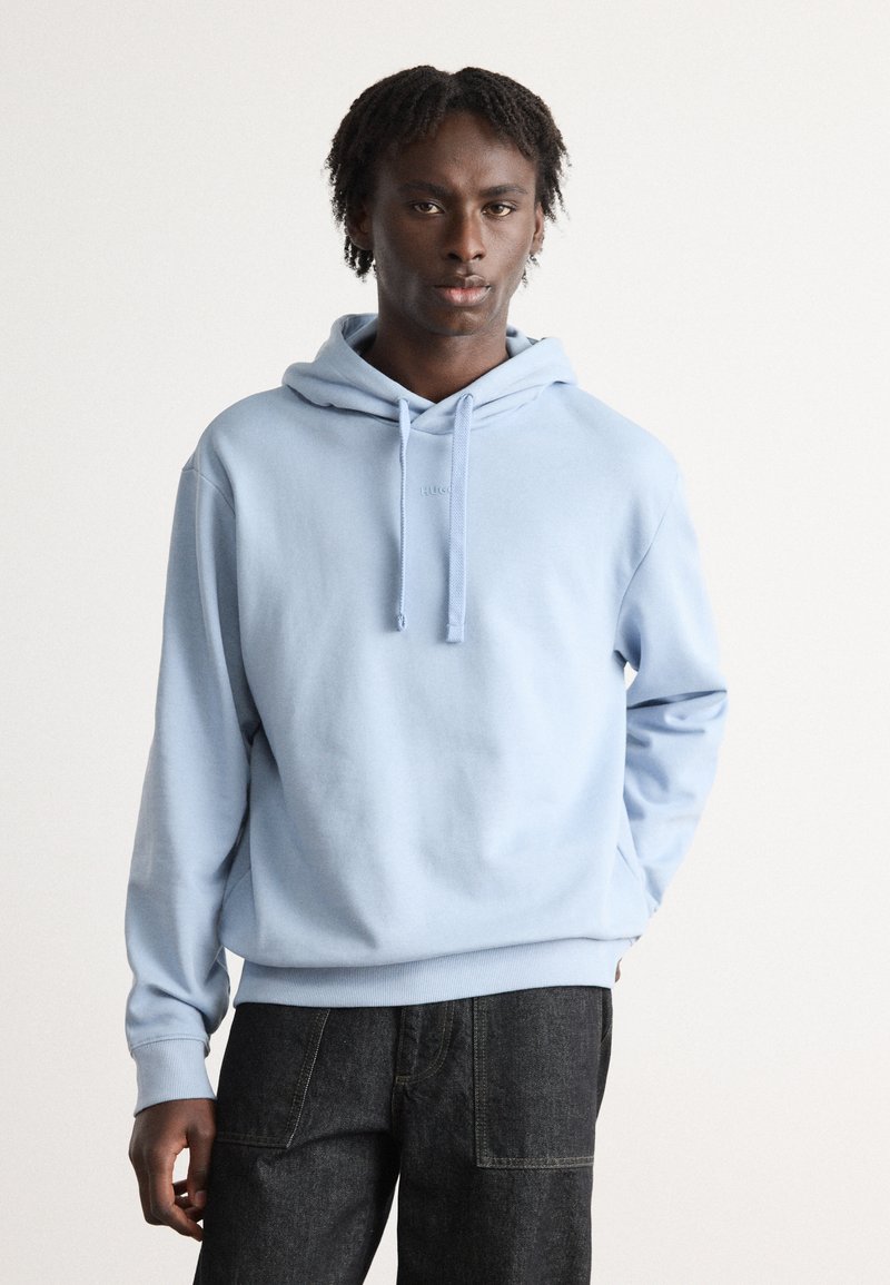 Sudadera azul claro con un bolsillo canguro en el frente, cordón ajustable y puños de canalé, combinada con jeans oscuros. Textura de tela suave.