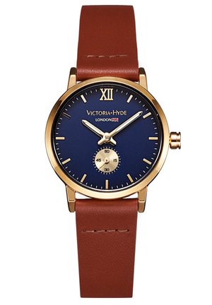 Personne portant un pantalon noir et des baskets blanches, avec une montre en cuir marron au poignet et un sac à main en cuir marron à côté d'elle.