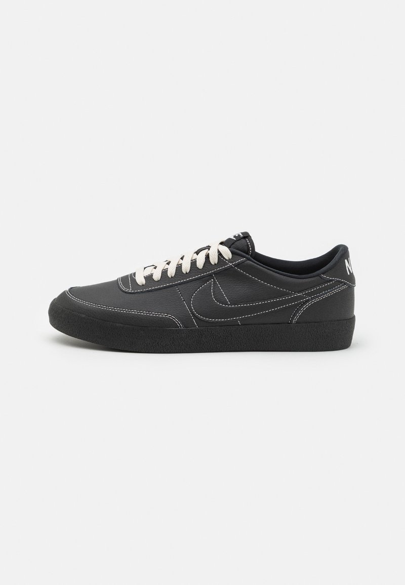 Fekete bőr sportcipők, texturált fekete gumitalppal, fehér varrással és krémszínű fűzővel. Nike logó látható az oldalon.