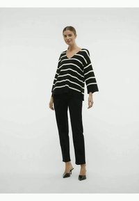 Top listrado em preto e branco com decote em V, mangas largas e fendas laterais, combinado com calças pretas slim e sapatos de salto finos pretos.