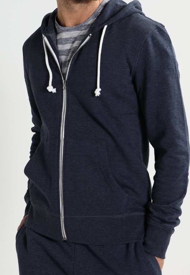 Sudadera con cremallera en color azul marino, fabricada en material suave, que cuenta con capucha ajustable, bolsillos frontales y un detalle de cremallera blanca en contraste.