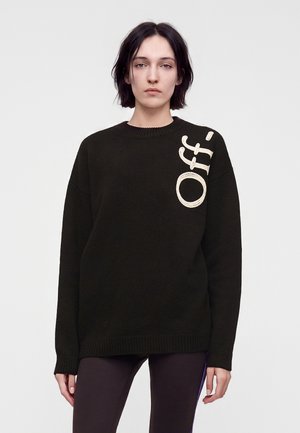 Ung person med kort mørkt hår iført en sort sweater med ordet "Off-" i store hvide bogstaver på øverste venstre side.