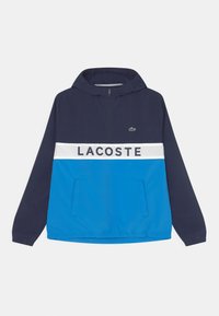 Chaqueta de pullover en azul marino con capucha, que cuenta con una franja blanca y el texto "LACOSTE" en el pecho. Tejido texturizado, con detalles de bolsillo.