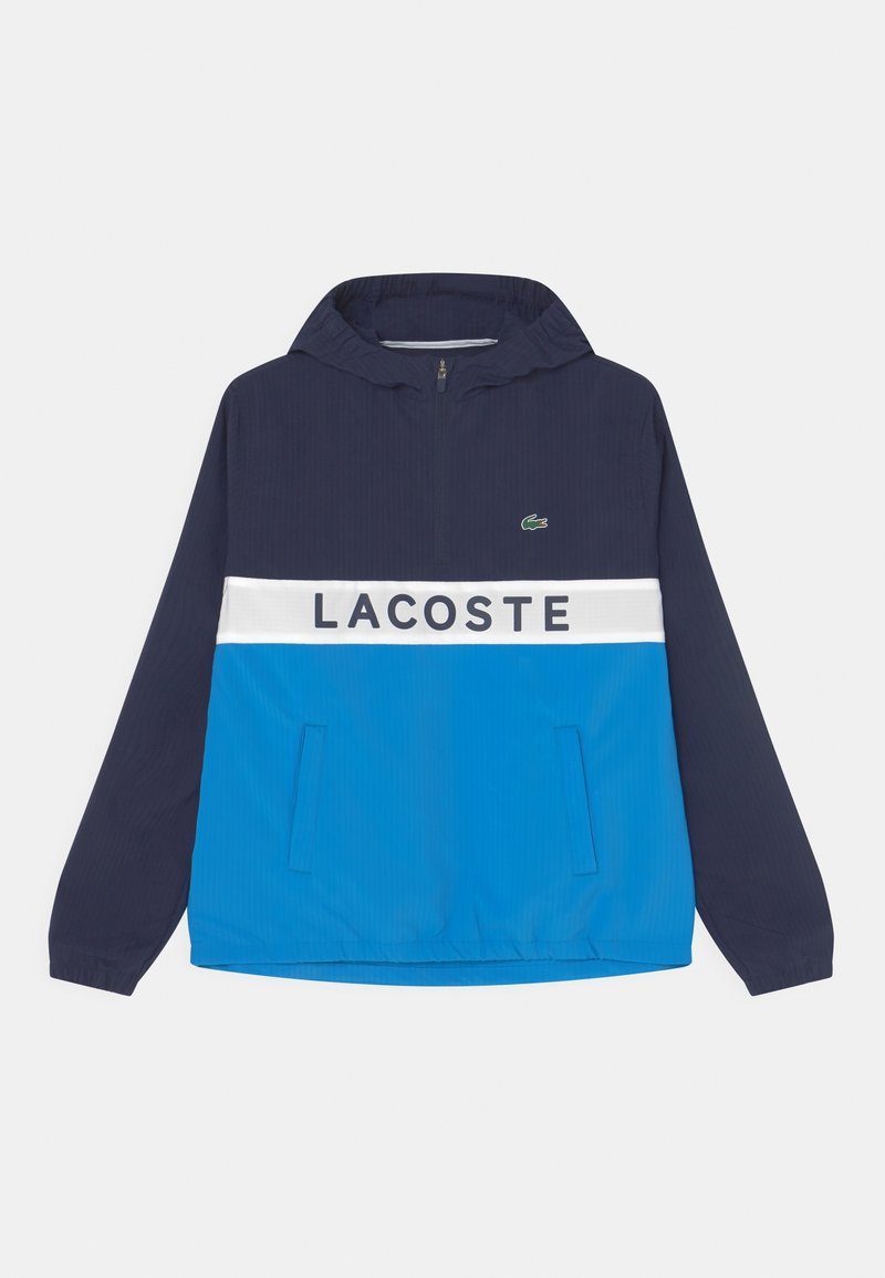 Chaqueta de pullover en azul marino con capucha, que cuenta con una franja blanca y el texto "LACOSTE" en el pecho. Tejido texturizado, con detalles de bolsillo.