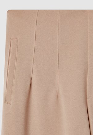 Pantaloni beige su misura con una texture liscia, dotati di tasche laterali e cuciture verticali per un aspetto strutturato.