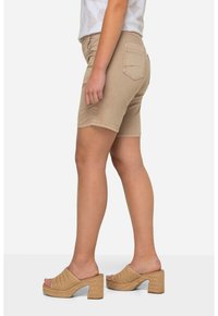 Shorts in denim beige con un design aderente, lunghezza a metà coscia e due tasche posteriori. Indossati con sandali a piattaforma intrecciati.