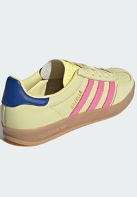 Žute kožne tenisice s ružičastim prugama, plavim petom i gumenom potplatom. Imaju perforirani jezik i brendirane detalje. Klasičan niskoprofilni dizajn.