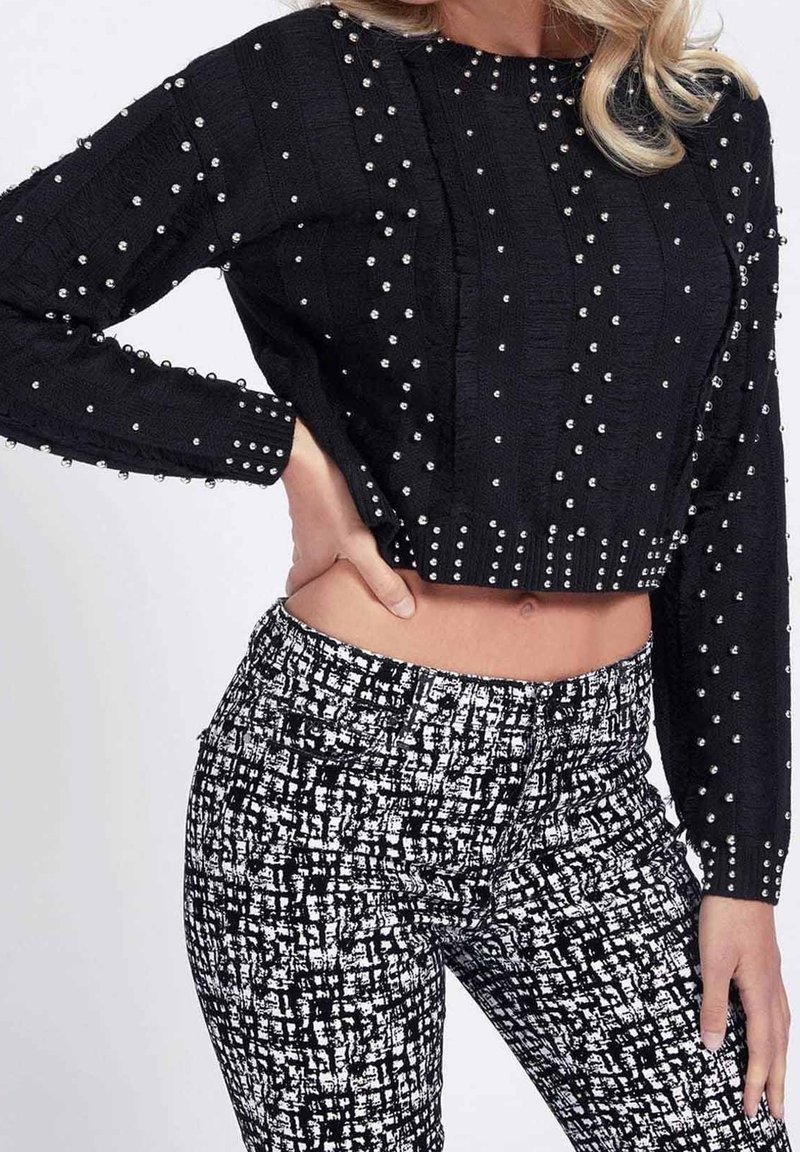 Czarny krótki sweter z teksturowanym wykończeniem i srebrnymi ćwiekami, w połączeniu z wysokim stanem czarno-białych spodni w wzory.