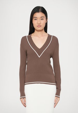 Brązowy prążkowany sweter z dekoltem w kształcie litery V, z białą lamówką przy kołnierzu i na dole oraz długimi rękawami. Miękka, dzianinowa faktura.