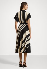 Melnā un bēšā svītraina kleita ar īsām piedurknēm, jostu viduklī un plūstošu svārku, kas nokrīt zem ceļgaliem. Gluda auduma tekstūra.