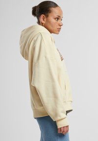 Felpa gialla realizzata in tessuto morbido, con un ampio cappuccio, spalle cadenti e polsini a costine. Indossata con denim, che mette in mostra un fit rilassato.