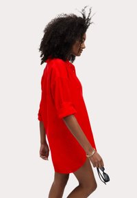 Abito camicia rosso realizzato in morbido tessuto, con colletto, maniche arrotolate e vestibilità ampia, con un orlo che arriva a metà coscia. Accessori non inclusi.