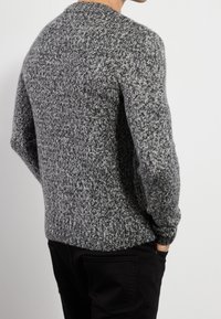 Grauer gestrickter Pullover mit einem strukturierten Muster, mit Rundhalsausschnitt und gerippten Manschetten, kombiniert mit schwarzen Hosen.