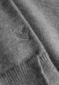 Grijze gebreide stof met een zachte textuur, voorzien van een klein, geborduurd hartdetail in een bijpassende kleur. Ribbelrand langs één kant.