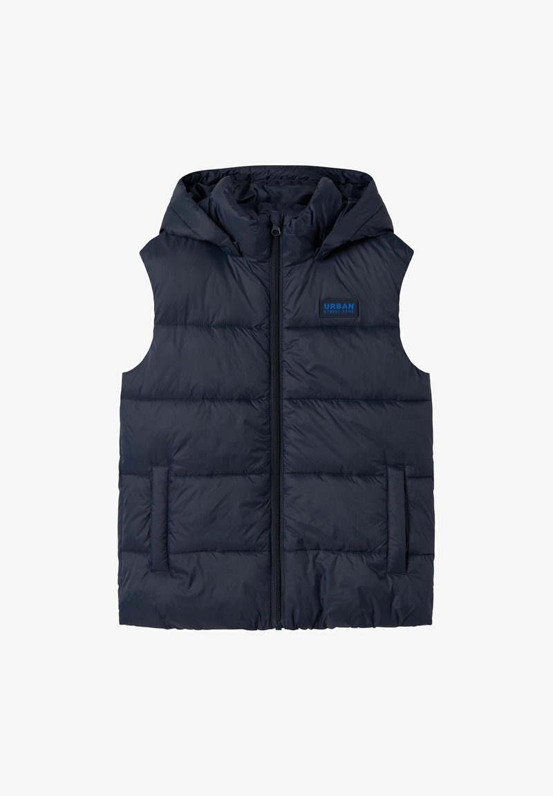 Chaleco acolchado azul marino con capucha, cierre de cremallera, dos bolsillos frontales y un parche con el logotipo en el pecho. Textura suave y diseño acolchado.