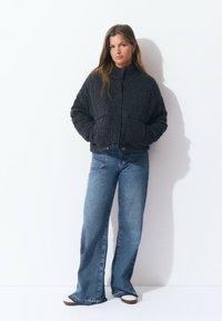 Veste bomber noire matelassée avec un col haut, des poignets élastiques et un ourlet élastique. Associée à un jean évasé bleu clair avec poches avant.