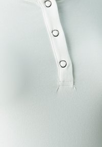 Top fixat de culoare verde deschis, dintr-un material texturat, cu un placket decorat cu accente de nasturi în tonuri de argint pe partea din față.