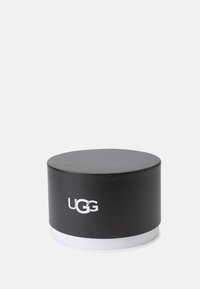 Černý cylindrický taburet s hladkým povrchem, bílý kulatý podstavec a výrazné logo UGG na boku.