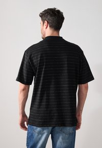 Sort kortærmet T-shirt med hvide vandrette striber, rund halsudskæring, afslappet pasform og blød stofstruktur.