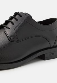 Pantofii eleganți din piele neagră au o textură netedă, vârful rotunjit și detalii minime de cusătură. Include șireturi negre și un logo embosat al brandului pe talpă.