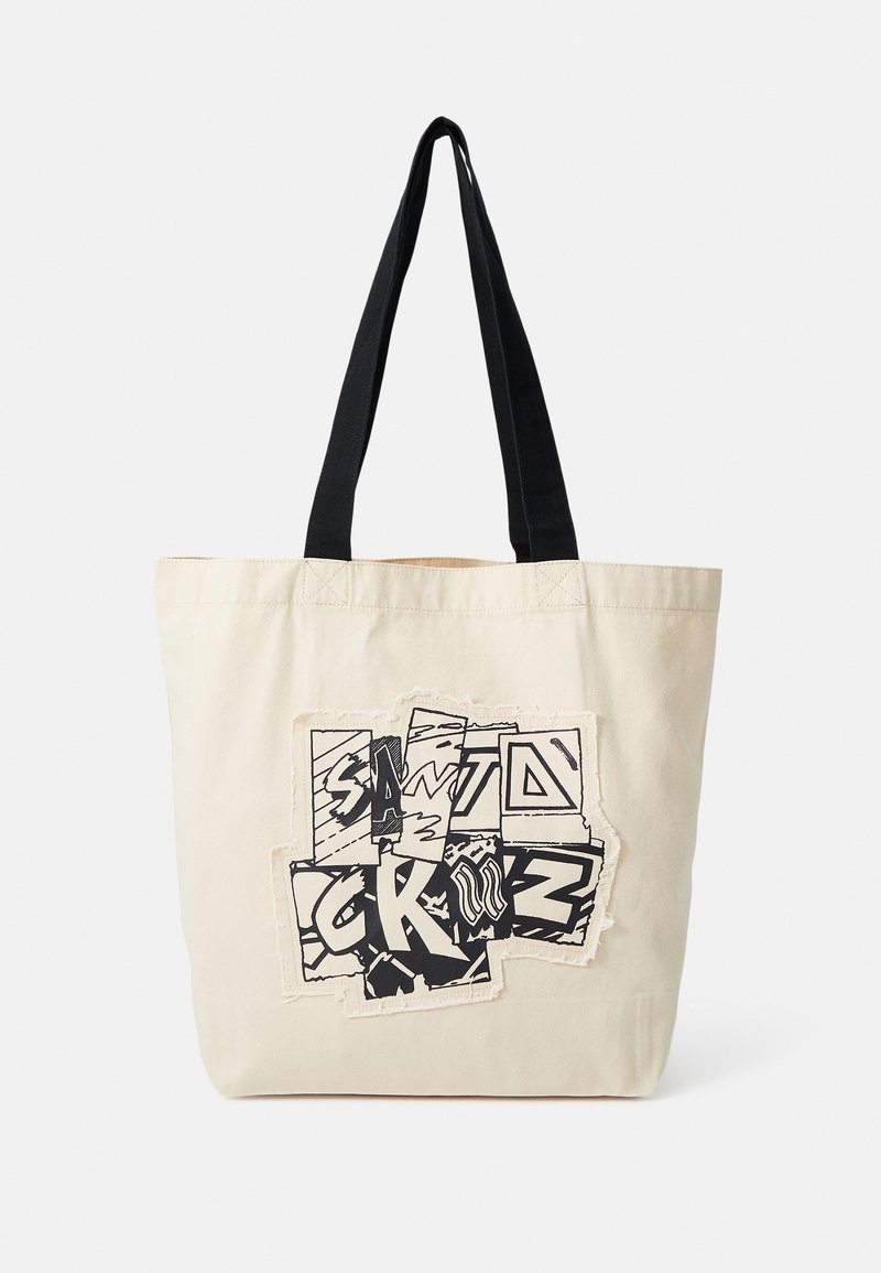 Sac tote en toile crème avec des poignées noires. Le devant présente un design graphique avec du texte et des motifs superposés, ajoutant texture et détail.