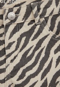 Zebra triibulise teksariide lähivõte mustade ja beežide triipudega, kus on näha vööaas, hõbedane nööp ja osa taskust.