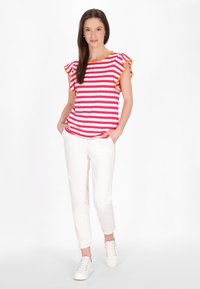 Roze en witte gestreepte T-shirt met gerimpelde mouwen en oranje accent, gecombineerd met witte tapered broek en witte sneakers.