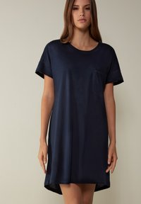 Abito corto blu navy a maniche corte con scollatura rotonda, tasca sul lato sinistro del petto, vestibilità comoda e orlo posteriore leggermente più lungo. Tessuto dalla texture liscia.