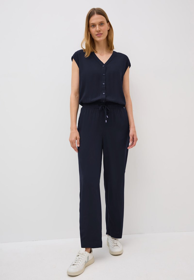 Marineblauw jumpsuit met een V-hals, korte mouwen, knopen aan de voorkant en een elastische taille. Heeft rechte benen en een strikdetail. Gekocht met witte sneakers.