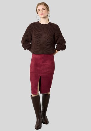 Donna che indossa un maglione a maglia grossa marrone scuro, una gonna a tubino in suede borgogna con spacco frontale e stivali alti fino al ginocchio in pelle marrone scuro.