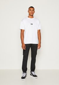 Witte katoenen T-shirt met een zwart "obey" logo, gecombineerd met zwarte cargobroeken en zwarte hoge sneakers met witte zolen.