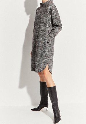 Vestito a quadri grigio con colletto alto e maniche lunghe, caratterizzato da una spacco laterale e tasche. Abbinato a stivali neri aderenti al ginocchio.