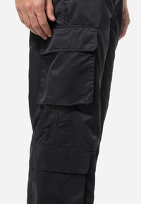 Black cargo pants in a smooth, lightweight fabric feature multiple side pockets and a tapered design, highlighting functional details.