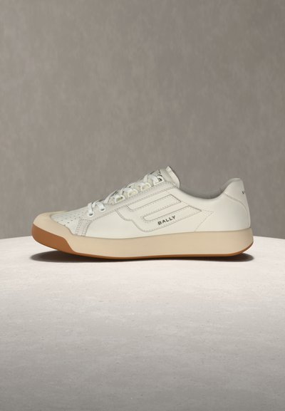 Baskets en cuir blanc avec semelle beige, bout perforé, lacets à l'avant et logo "BALLY" sur le côté et le talon, posées sur une surface claire.