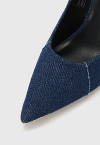Chausseur à bout pointu pour femmes recouvert de tissu en denim bleu foncé avec des coutures visibles et une doublure intérieure noire.