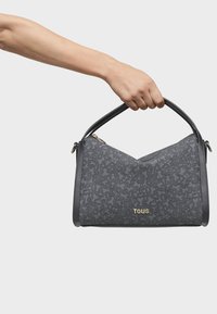 Szara torebka z teksturowanym wzorem, złotym logo marki i podwójnymi skórzanymi uchwytami. Posiada trójkątny kształt i złote zapięcie na zamek.