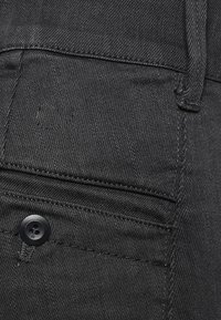 Tejido de mezclilla negra con una textura suave, que presenta detalles de costura, un acento de botón y un bolsillo.