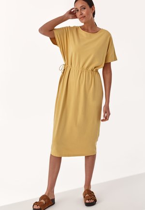Yellow short-sleeve dress with an elastic drawstring waist, knee-length hem, smooth texture, paired with brown slide sandals.