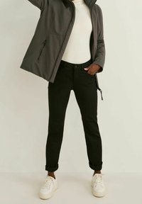 Šedá bunda na zip, nošená přes bílý žebrovaný svetr. Černé úzké kalhoty s ohrnutými manžetami v kombinaci s bílými teniskami.