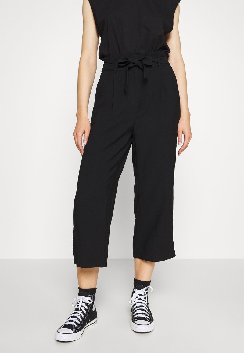 Pantalon court noir taille haute avec ceinture à nouer et coupe ample, associé à des baskets montantes noires et blanches.