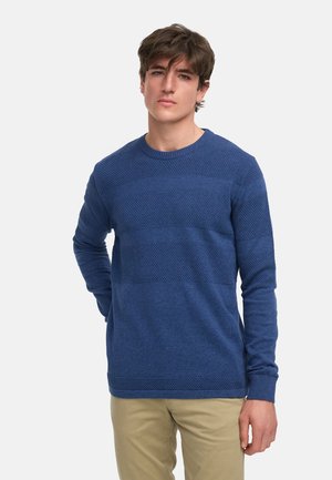 Suéter de punto azul con rayas horizontales texturizadas. Presenta un escote redondo y mangas largas, combinado con pantalones de color claro.