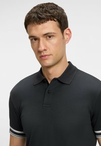 Svart polo t-shirt med krage, tvåknappars knappslå och kontrasterande randiga ärmar i grått och vitt. Slät bomullstyg.