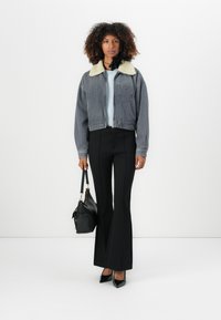 Cropped denim jacket with a cream shearling collar, vertical blue stripes, paired with black flared pants and a black handbag.