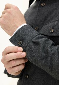 Gray wool shirt with buttoned cuffs. Features black buttons and a textured fabric. Cuff overlaps white inner layer.