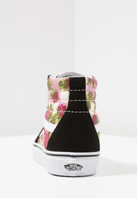 Baskets montantes avec un motif floral en rose, vert et blanc, présentant des accents en suède noir et une semelle en caoutchouc blanc.